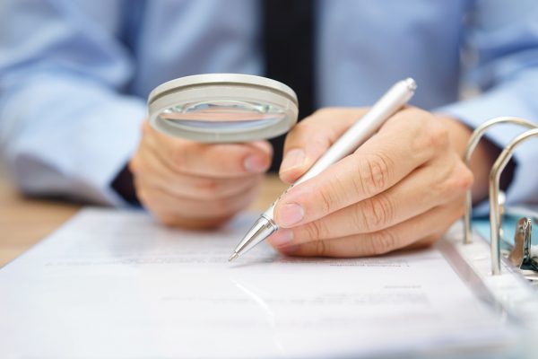 businessman is analyzing through magnifying glass contract and