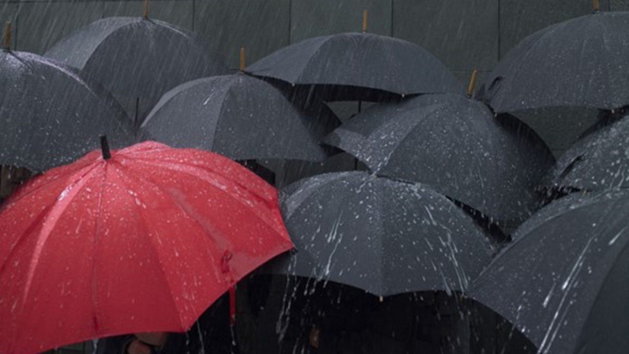 Red umbrella amongst group of open umbrellas in rain