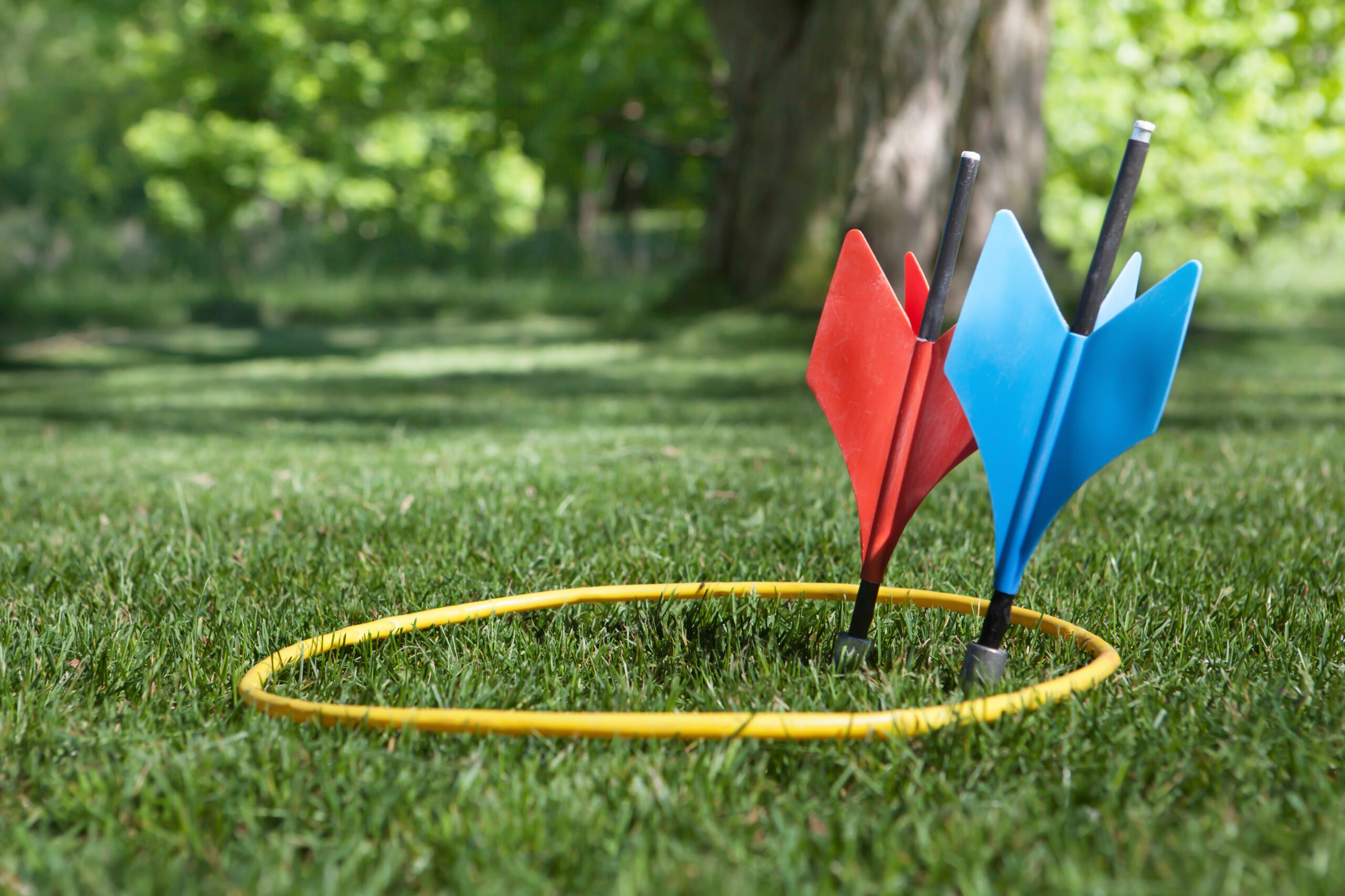 a shot of some vintage lawn darts sometimes called JARTS. One of each color inside the yellow ring in a back yard setting.