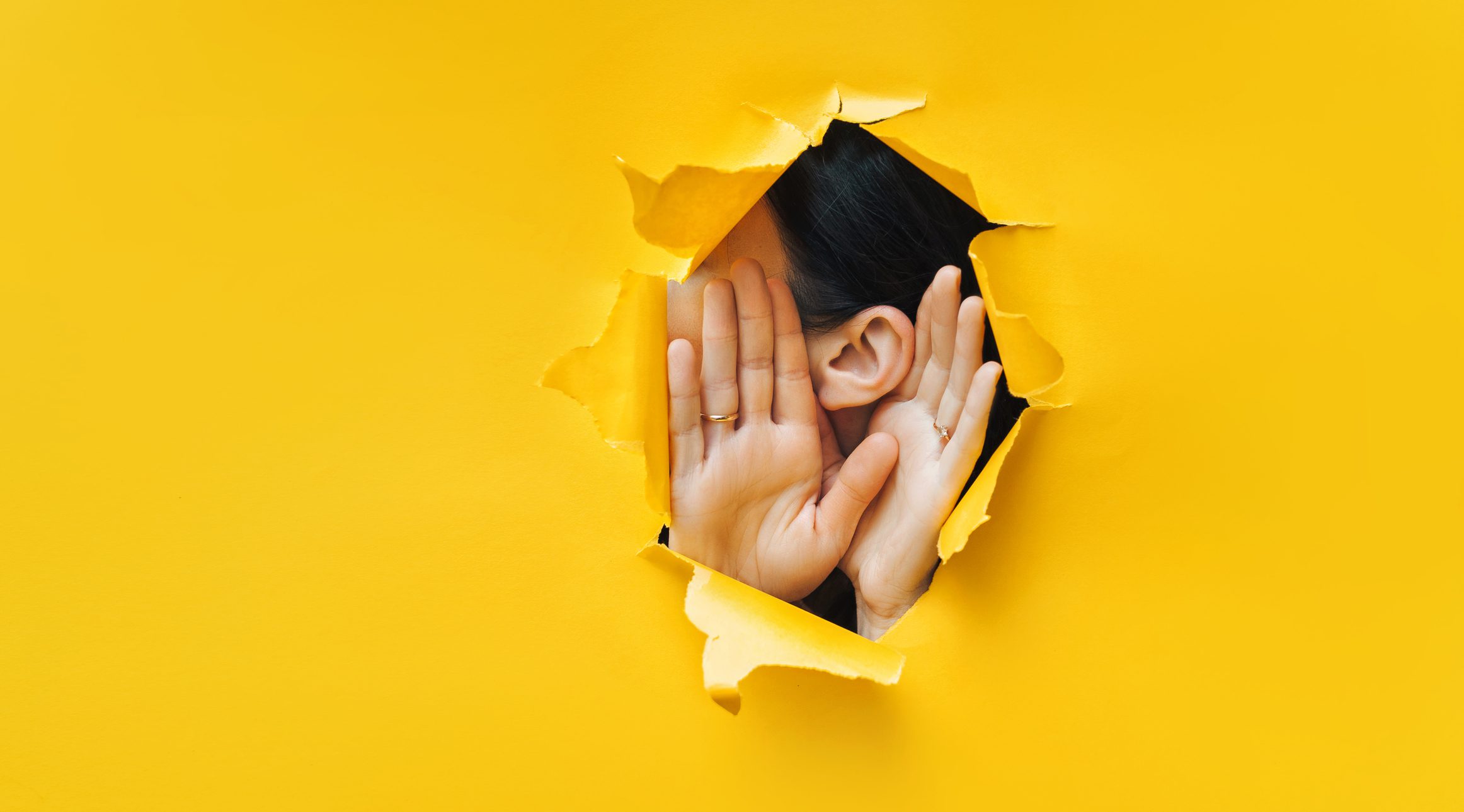 Female ear and hands close-up. Torn paper, yellow background.